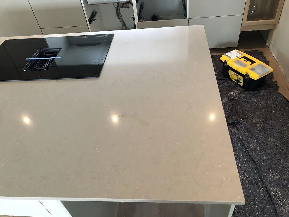 Ovanifrån av köksö i Silestone Coral Clay med induktionshäll och nedfälld fläkt, varm gråbeige kvartskomposit i ett kök i Sölvesborg.