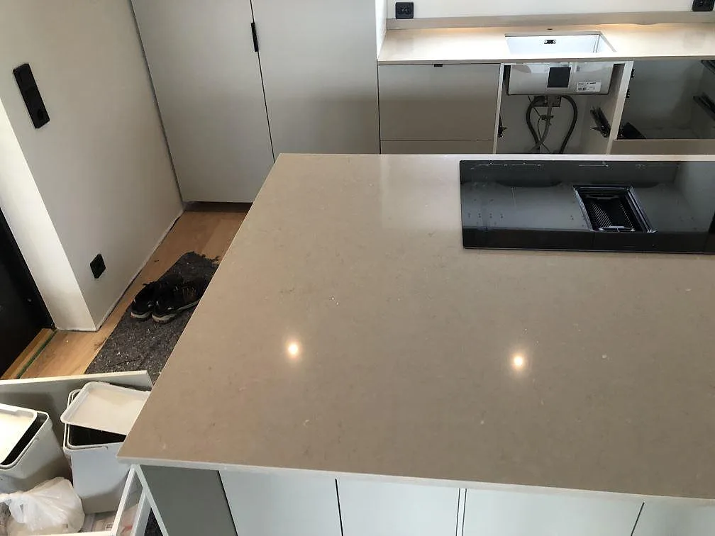 Hörn av köksö och vägghängd bänkskiva i Silestone Coral Clay med induktionshäll och diskhostans i ett kök under montering i Sölvesborg.