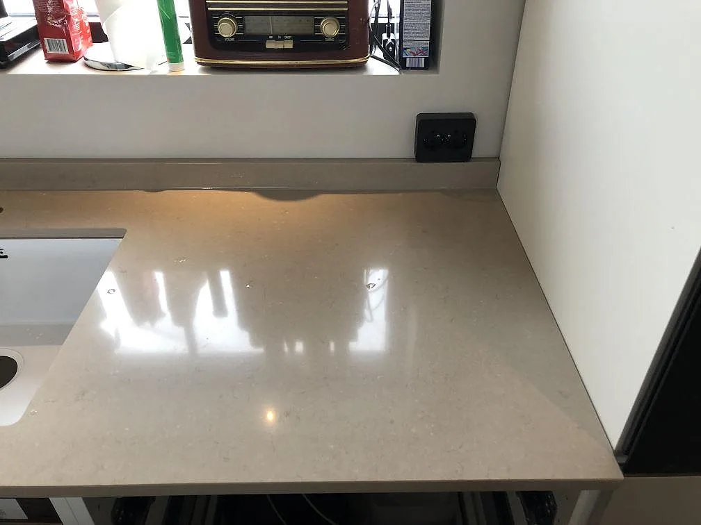 Polerad bänkskiva i Silestone Coral Clay med underlimmad vit diskho och låg uppvikt stänkkant mot fönstret i ett kök i Sölvesborg.