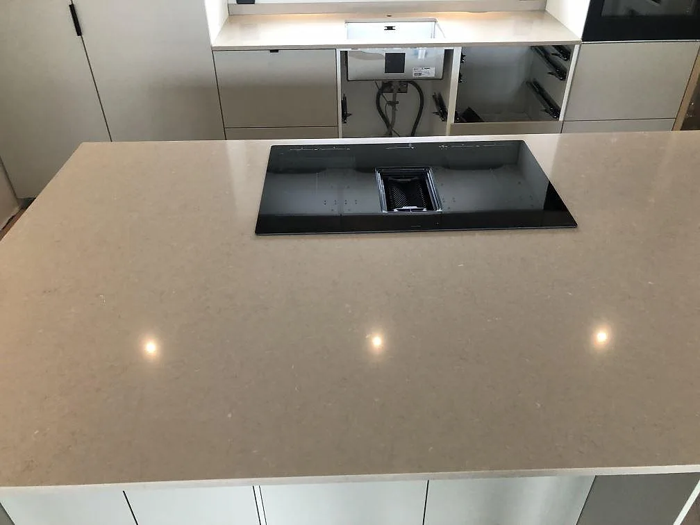 Köksö i Silestone Coral Clay i ett kök i Sölvesborg, med nedfälld induktionshäll och fläkt och bänkskiva med diskhostans i bakgrunden.