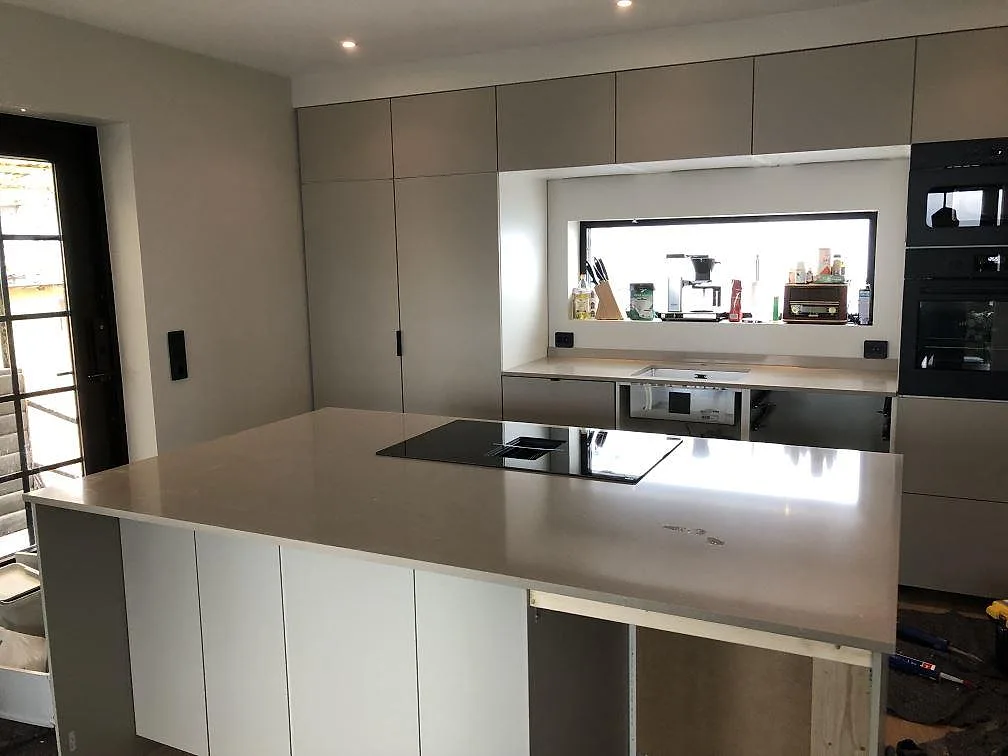 Köksbänkskiva och köksö i Silestone Coral Clay, en varm gråbeige kvartskomposit, med integrerad induktionshäll i ett kök under montering i Sölvesborg.