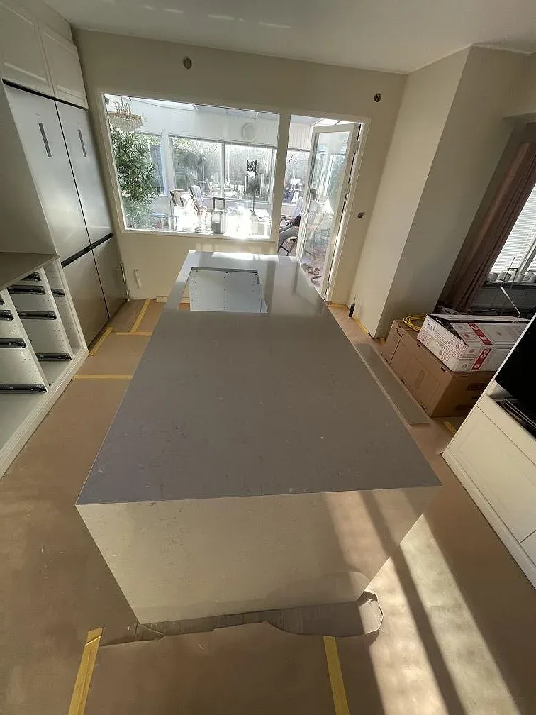 Brett vy över kök i Silestone Coral Clay med köksö och stort fönster under montering i Sölvesborg.