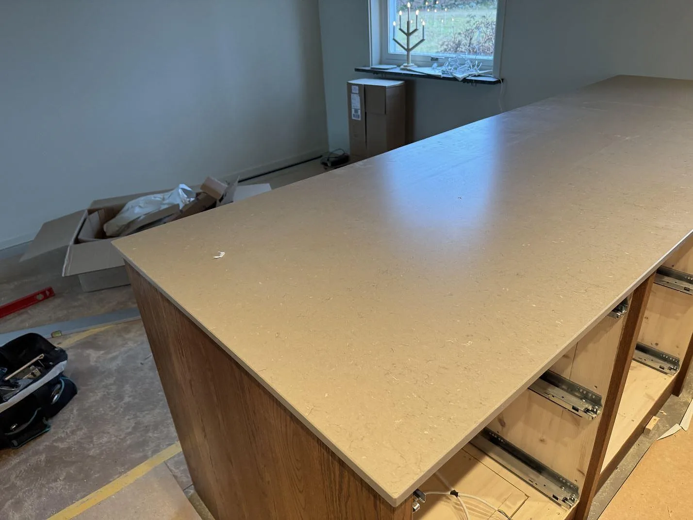 Stor köksö i matt Silestone Coral Clay, 20 mm kvartskomposit, monterad på trästommar under köksmontering i Sösdala.