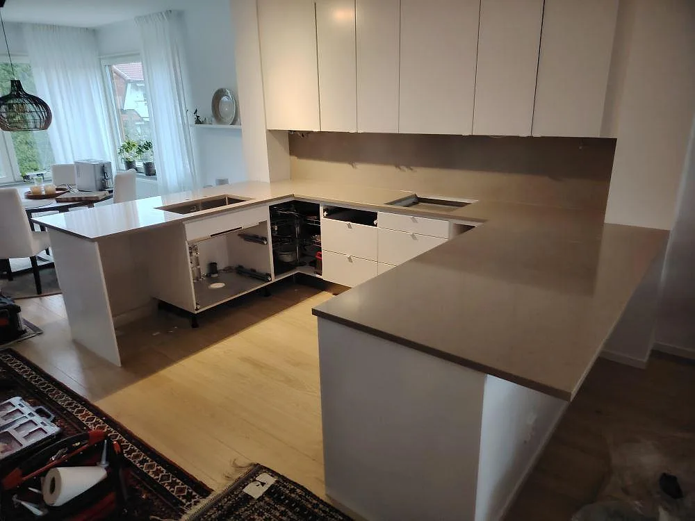 Polerad kompositbänkskiva i Silestone Coral Clay med halvö, ljusa stommar och väggskiva under överskåp i Sollentuna.