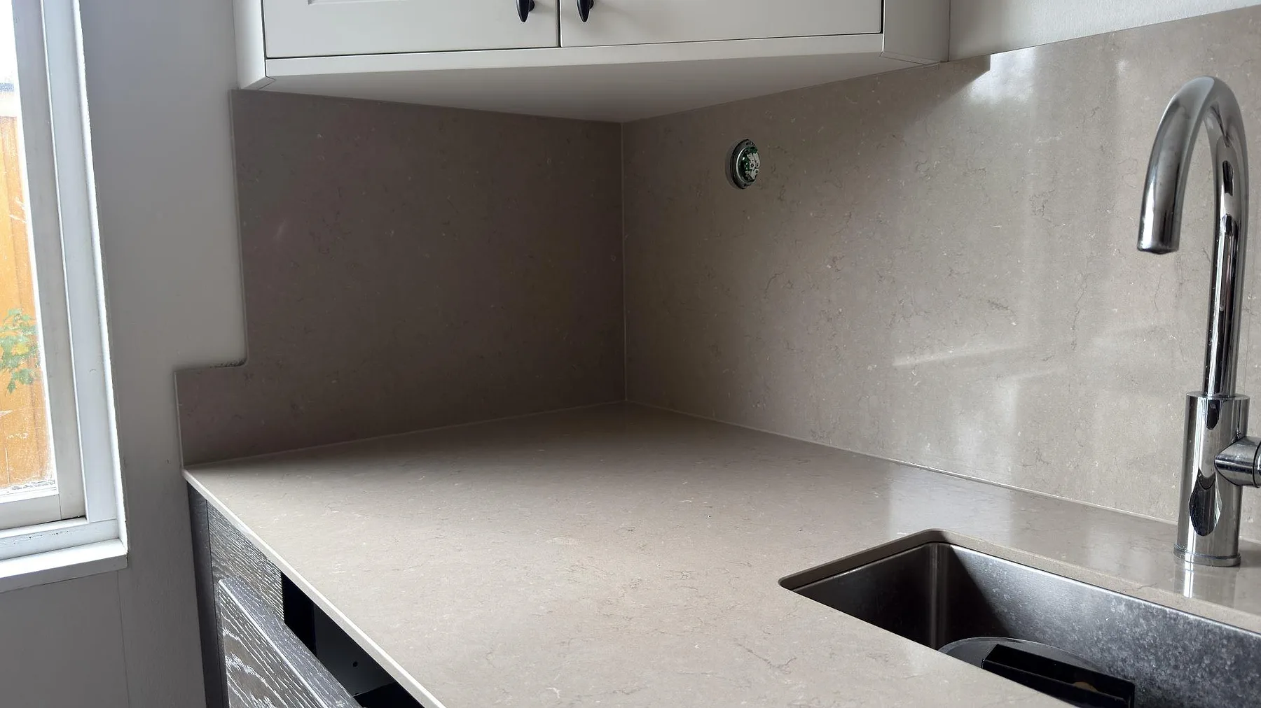 Köksbänkskiva i Silestone Coral Clay i Sollentuna med hörnvinkel på stänkväggen i samma sten, fönster och underlimmad rostfri diskho.