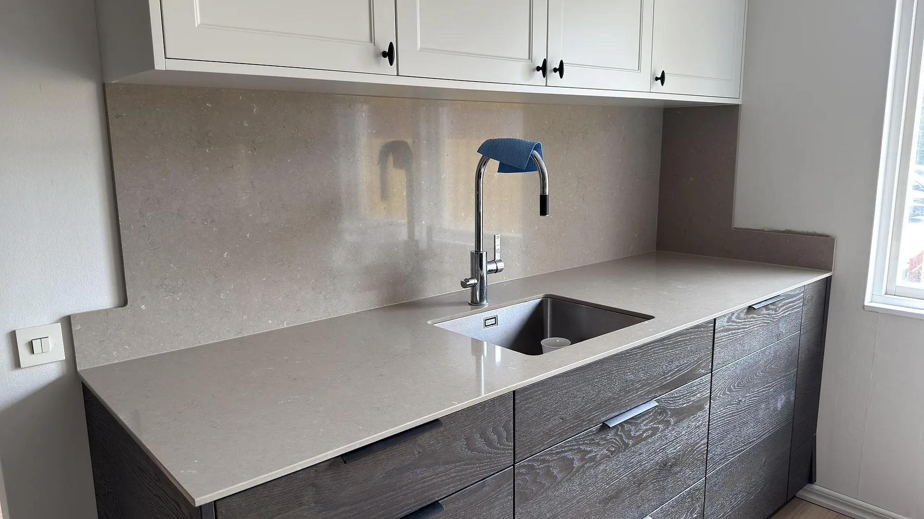 Köksbänkskiva i Silestone Coral Clay, polerad varm greige komposit, med underlimmad rostfri diskho och heltäckande stänkvägg i samma sten mot mörka ekluckor i ett kök i Sollentuna.