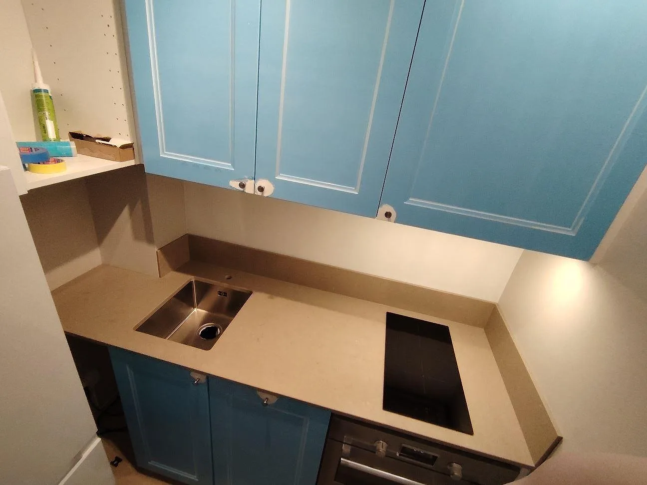Köksbänkskiva i greige Silestone Coral Clay, polerad kvartskomposit, med underlimmad rostfri diskho, induktionshäll och stänkskydd i ett blått kök i Solna.