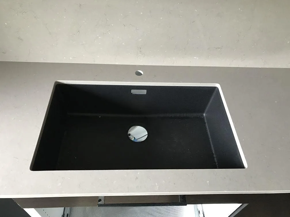 Närbild på köksö i Silestone Coral Clay med underlimmad svart kompositdiskho och borrhål för blandare i ett kök i Staffanstorp.