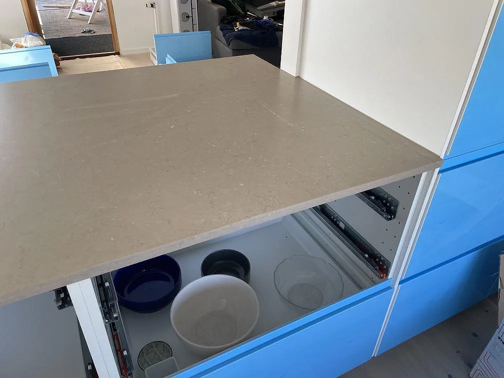 Köksö i Silestone Coral Clay med matt greigebeige yta och öppna blå lådstommar i ett kök i Staffanstorp.