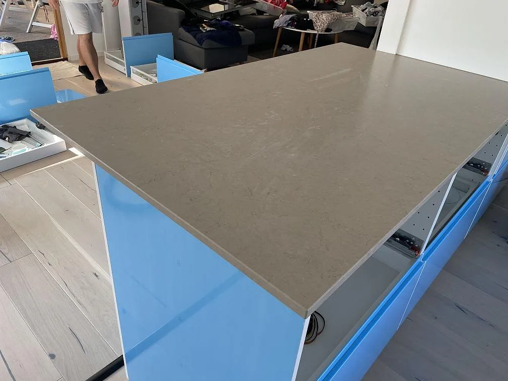 Närbild av den stora köksön i matt Silestone Coral Clay, 20 mm komposit, på blå skåp under montering i Staffanstorp.