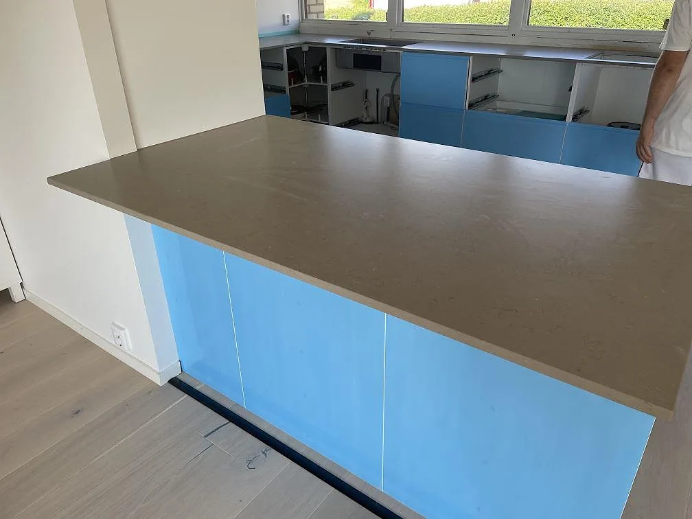 Stor köksö i matt Silestone Coral Clay, greigebeige komposit, med blå skåp och fönsterrad i ett kök i Staffanstorp.