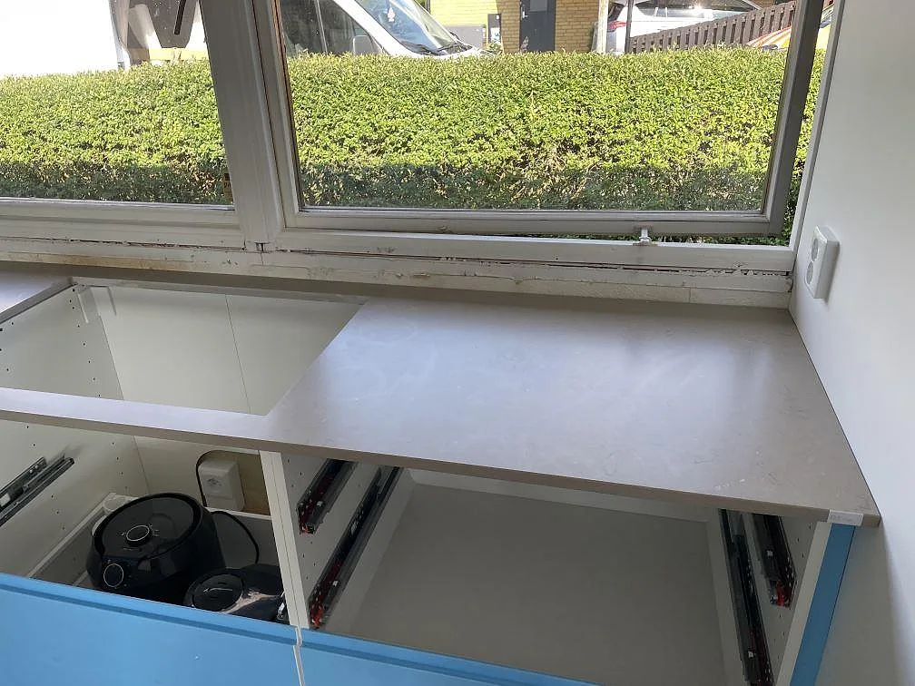 Bänkskiva i matt Silestone Coral Clay vid fönster med öppning för underlimmad diskho och blå skåp i Staffanstorp.
