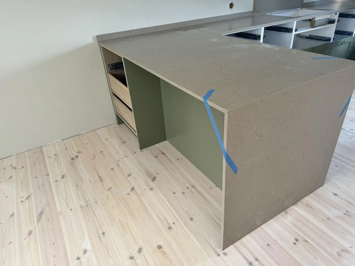 Köksbänkskiva i matt Silestone Coral Clay komposit på köksö med neddragen stensida, grön nederinredning och ljust trägolv i Stenkullen.
