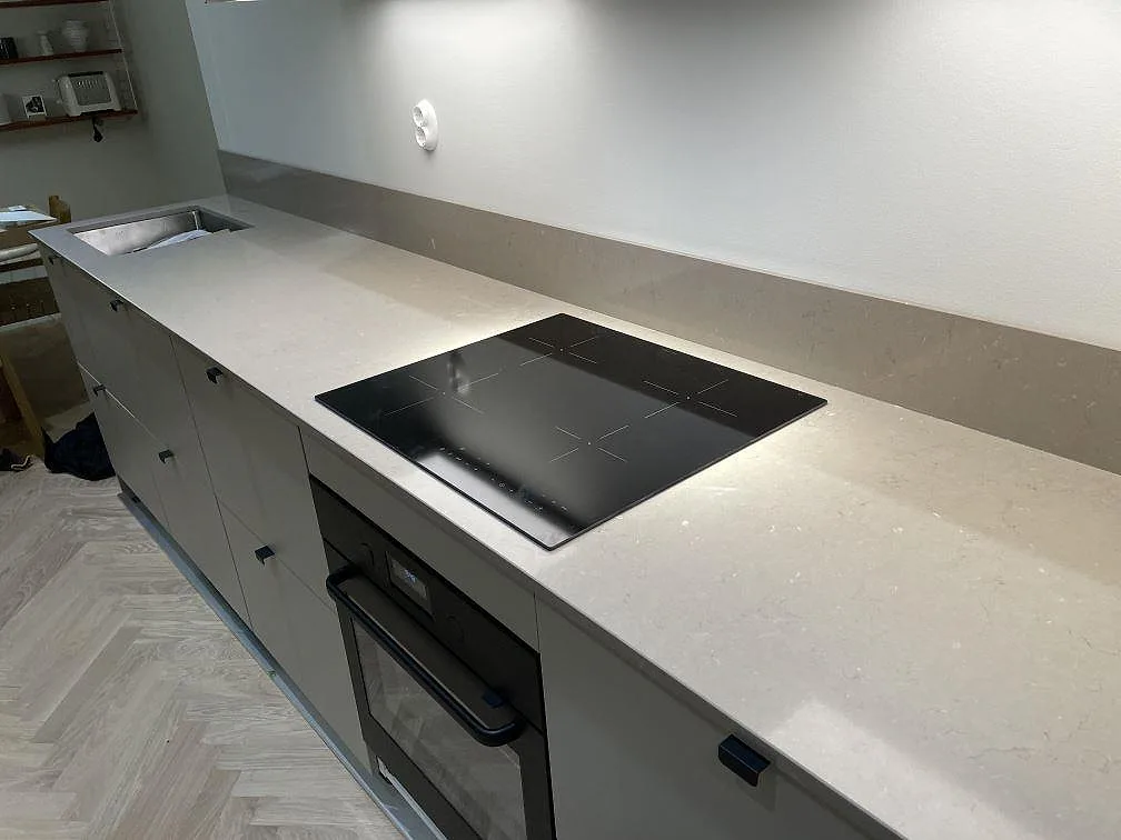 Polerad bänkskiva i Silestone Coral Clay med induktionshäll, ugn och matchande stänkskydd mot grå köksluckor i Stockholm.