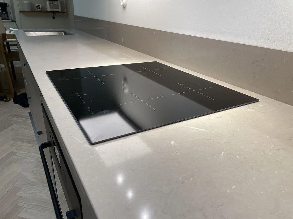 Närbild på polerad Silestone Coral Clay runt hällen, med varm gråbeige komposityta och stänkskydd i ett kök i Stockholm.