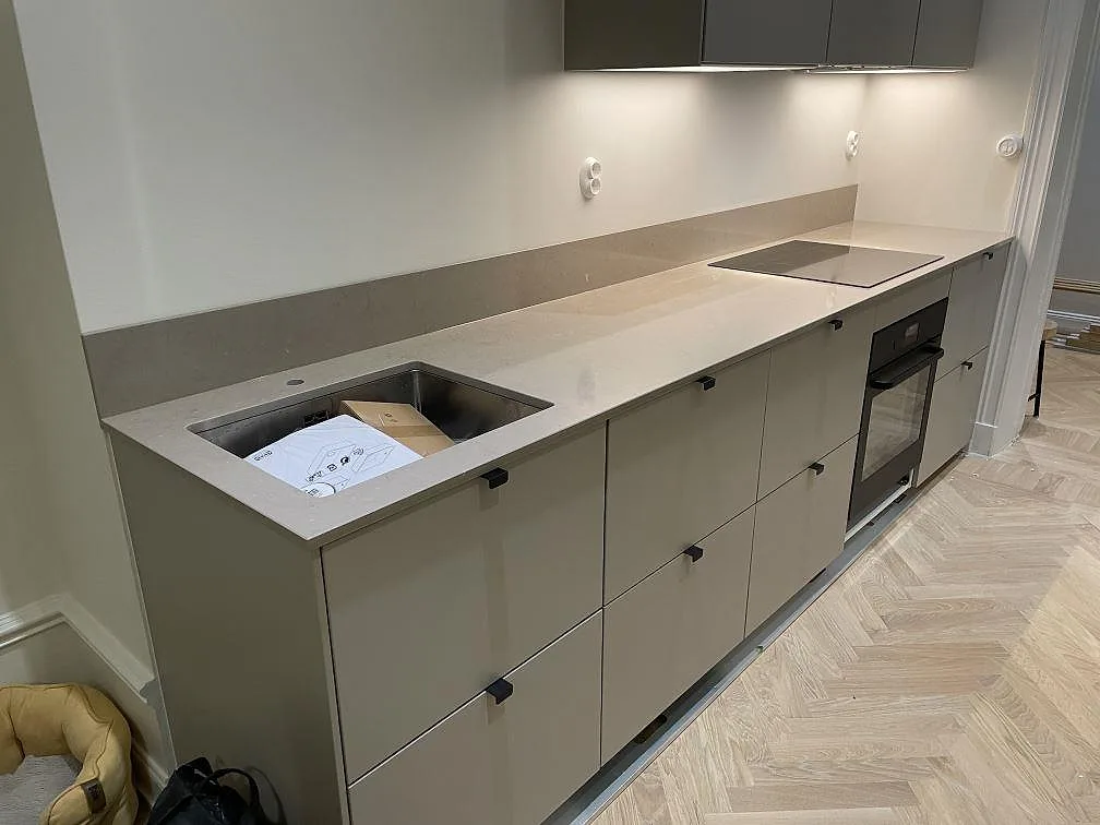 Köksbänkskiva i greige Silestone Coral Clay, polerad, med underlimmad rostfri diskho, häll och stänkskydd i ett kök i Stockholm.