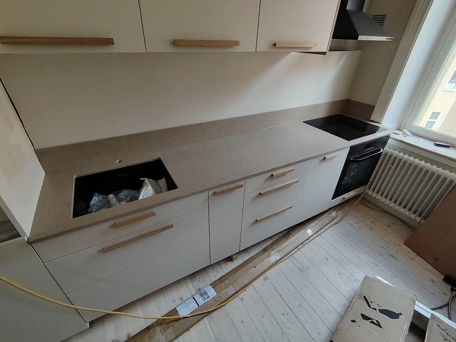 Rak köksbänkskiva i matt Silestone Coral Clay komposit med diskhoöppning, svart häll och låg stänkkant i ett kök i Stockholm.