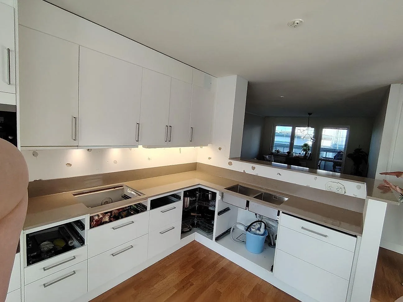 U-format kök i Stockholm med polerad Silestone Coral Clay som bänkskiva och uppvikt stänkskydd under vita överskåp.