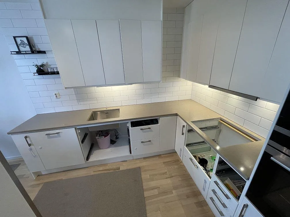 Polerad Silestone Coral Clay bänkskiva i kvartskomposit längs två väggar i ett vitt kök under montering i Stockholm.