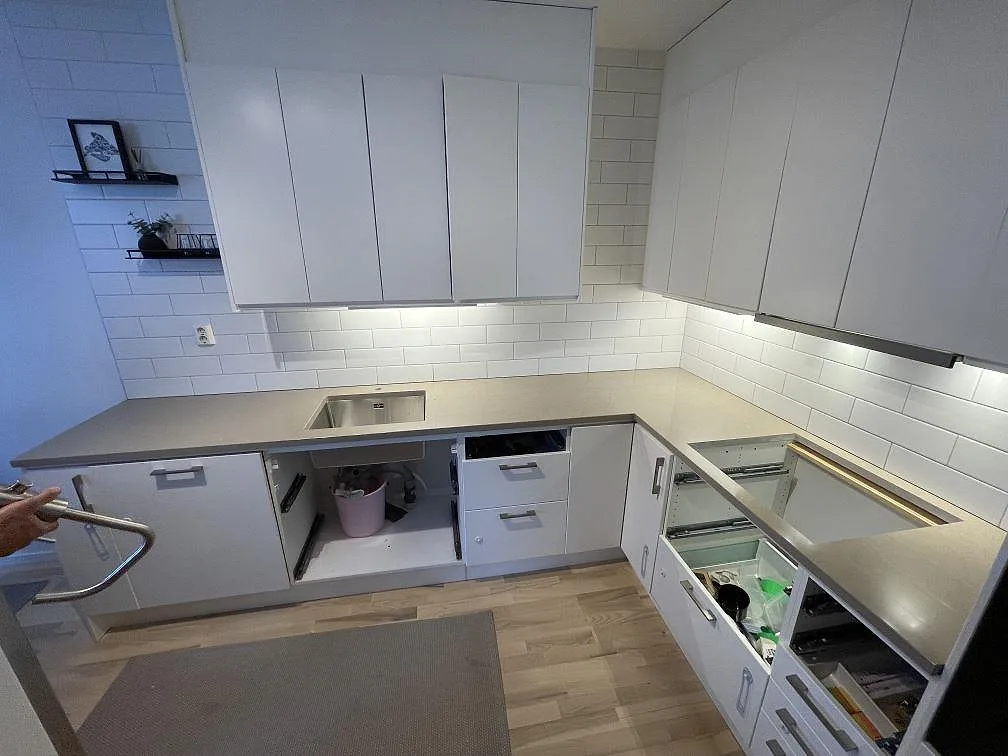 Köksbänk i 30 mm polerad Silestone Coral Clay med gråbeige yta, kaklad vägg och öppna lådor under montering i Stockholm.