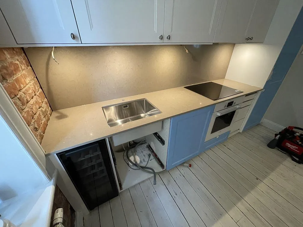 Lång köksbänkskiva i polerad Silestone Coral Clay med diskho, häll och överskåp under montering i Stockholm.