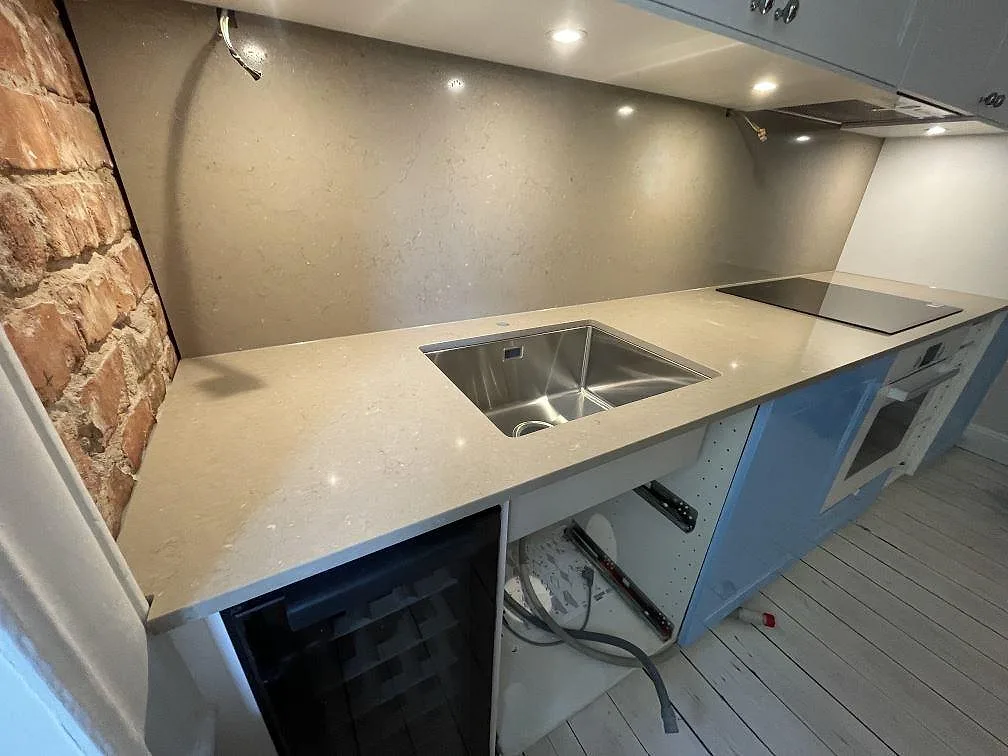 Närbild på köksbänkskiva i polerad Silestone Coral Clay med rostfri diskho och stenklädd vägg i Stockholm.