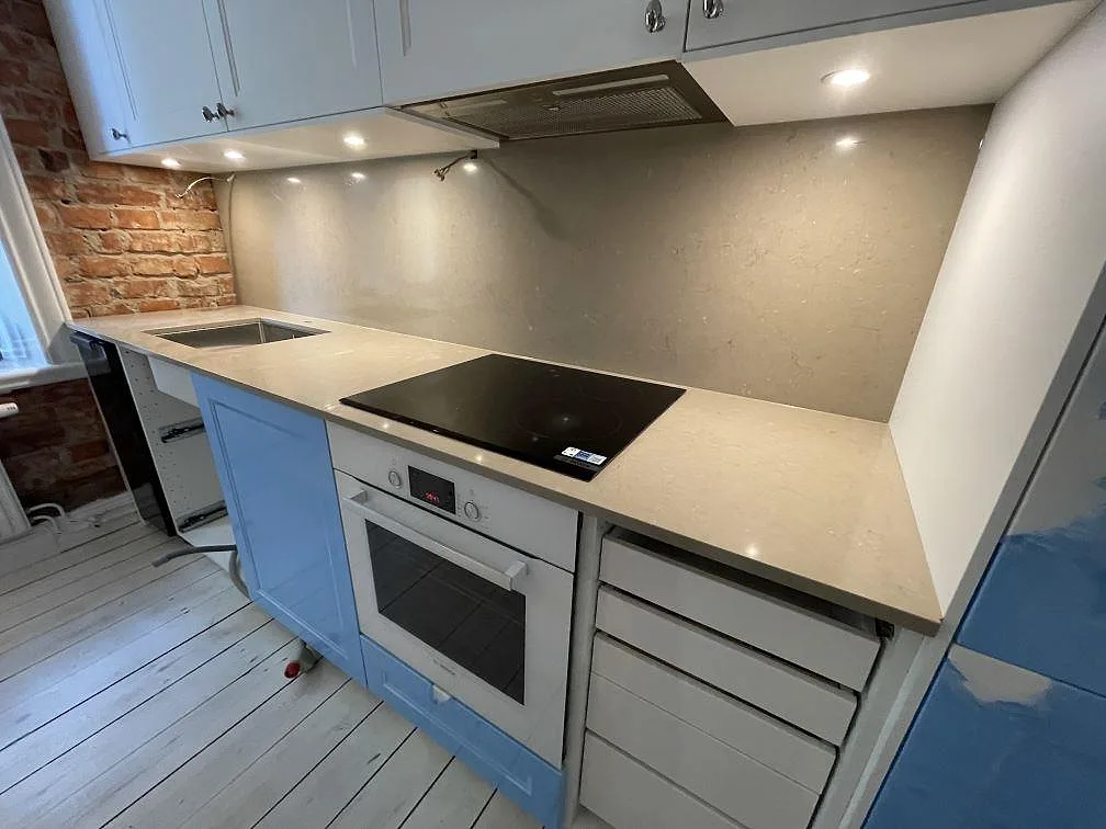 Polerad Silestone Coral Clay runt häll och rostfri diskho med hög väggsten i ett kök i Stockholm.