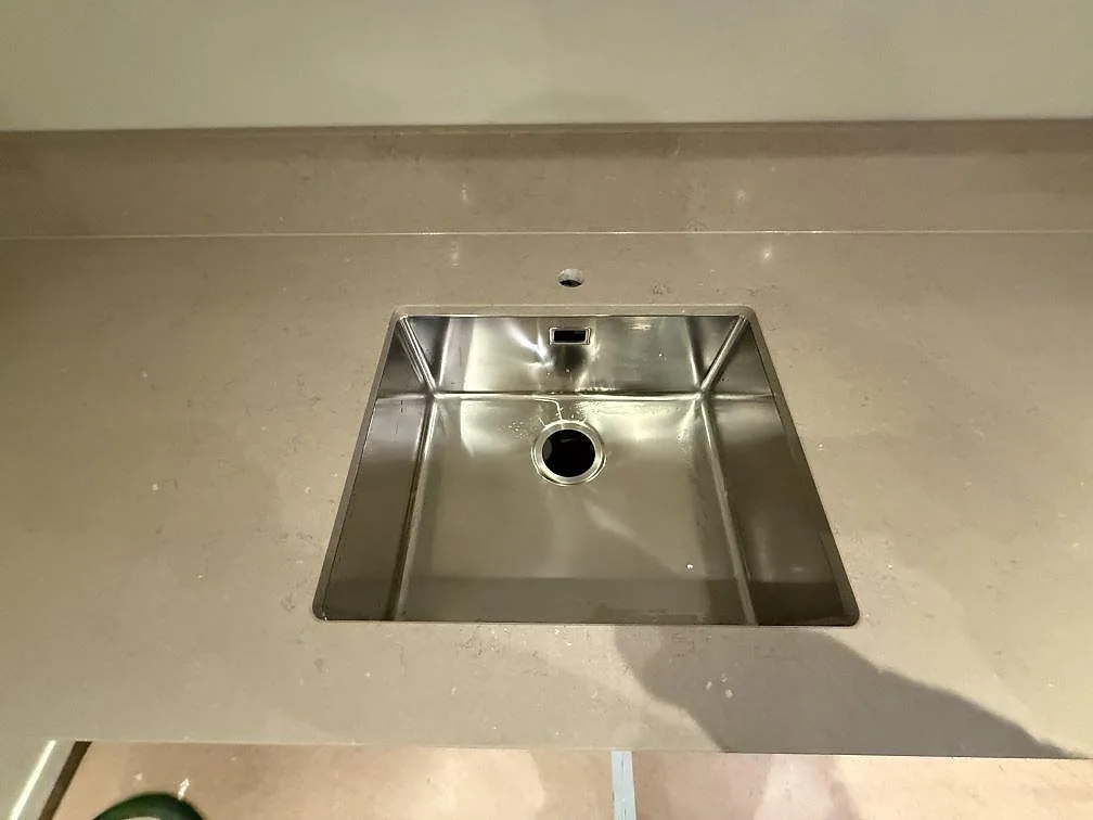 Detalj av polerad Silestone Coral Clay komposit med rostfri diskho, blandarhål och uppvikt stänkkant i Stockholm.