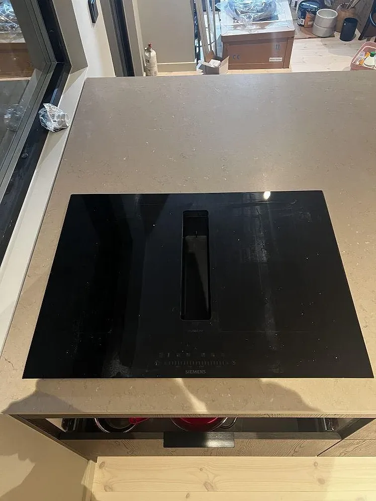 Svart induktionshäll i en matt köksbänkskiva av Silestone Coral Clay vid stora fönster i Strömstad.