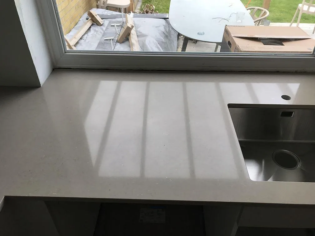 Köksbänkskiva i Silestone Coral Clay vid fönstret med underlimmad rostfri diskho och förborrat blandarhål i ett kök i Svalöv.