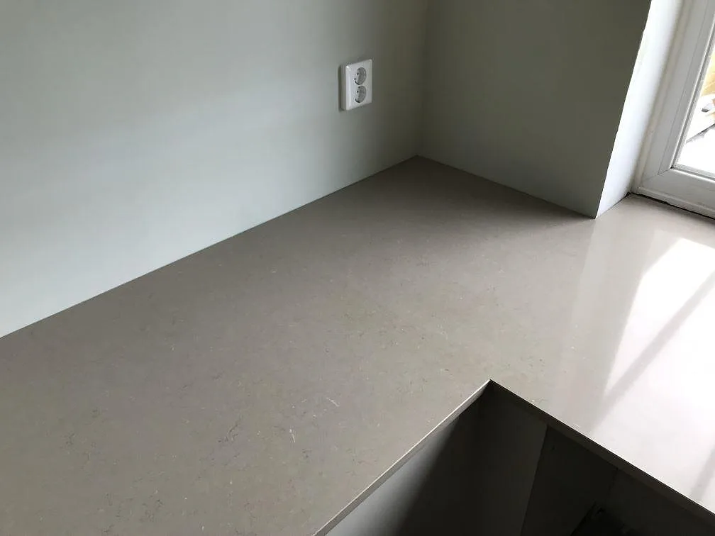 Hörnparti av köksbänkskiva i Silestone Coral Clay, polerad varm greige kvartskomposit, vid ett fönster i ett kök i Svalöv.