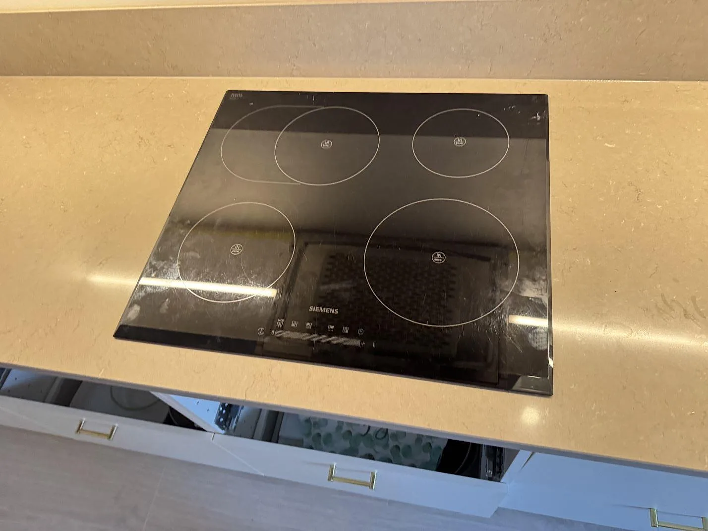Närbild på svart häll monterad i en polerad Silestone Coral Clay köksbänkskiva i komposit i Svedala.