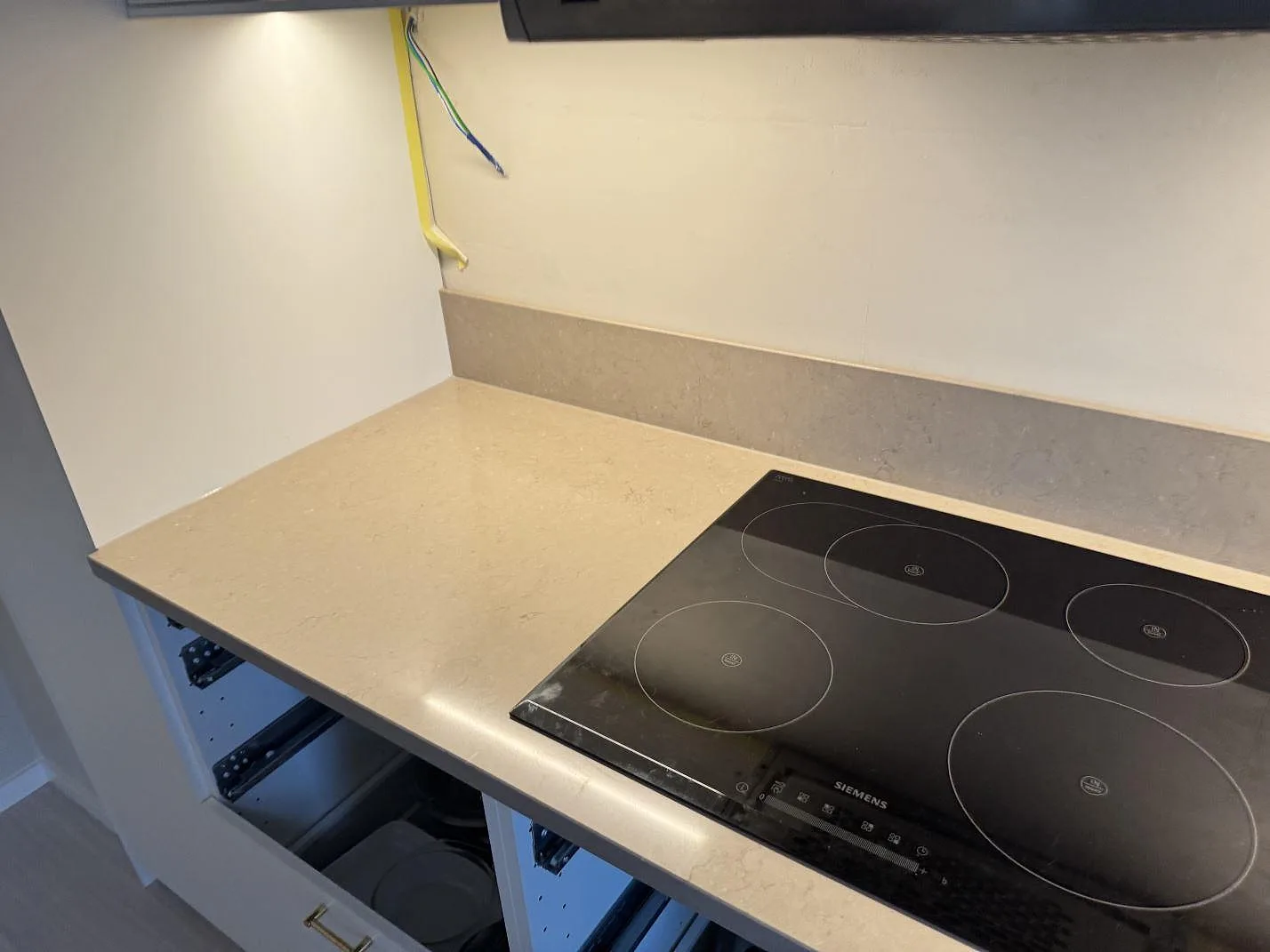 Köksbänkskiva i beigegrå Silestone Coral Clay, polerad, med svart häll och stänkkant i ett kök under montering i Svedala.