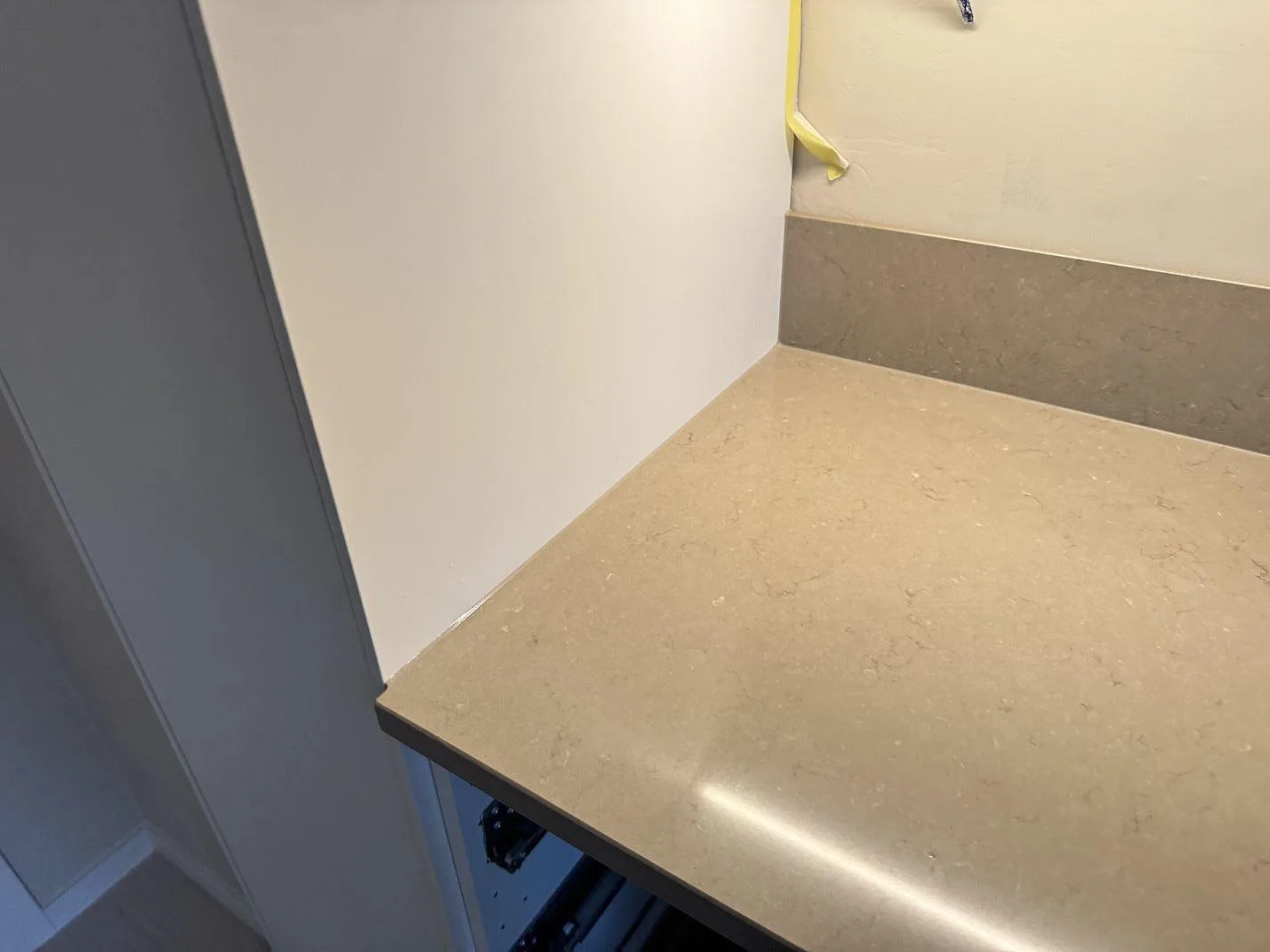 Detalj av polerad Silestone Coral Clay bänkskiva i beigegrå komposit med stänkkant och sidovägg i ett kök i Svedala.