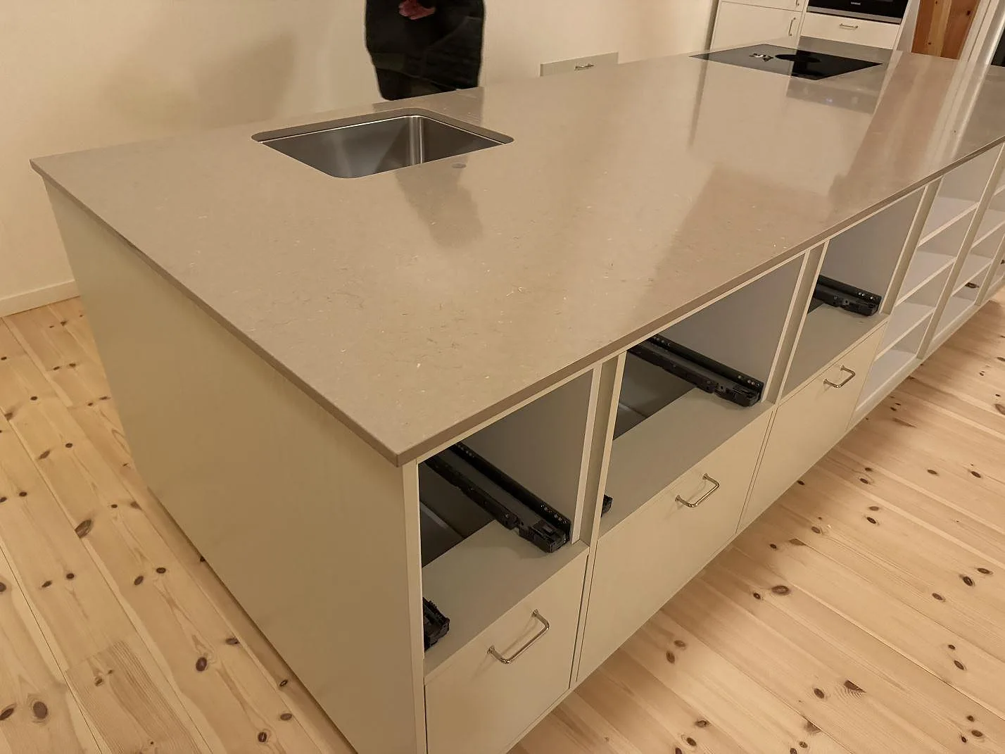 Polerad bänkskiva i Silestone Coral Clay över köksö med rostfri diskho och öppna lådsektioner under montering i Svendborg.