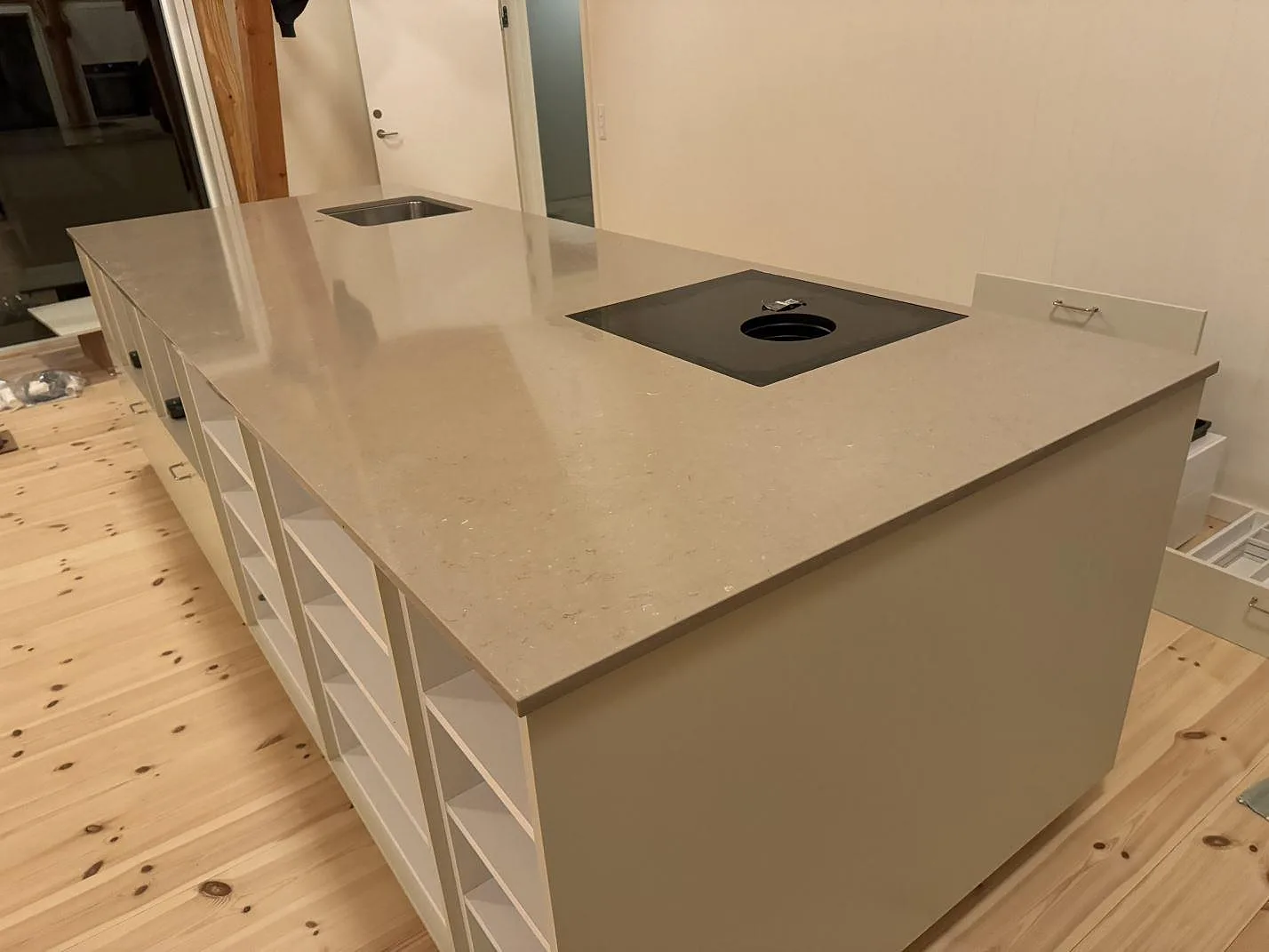 Lång köksö i polerad Silestone Coral Clay med infälld häll, underlimmad rostfri diskho och ljusa köksstommar i Svendborg.