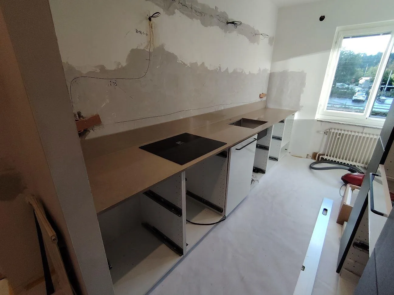 Köksbänkskiva i polerad Silestone Coral Clay, en varm gråbeige komposit, med häll i ett kök under montering i Täby.