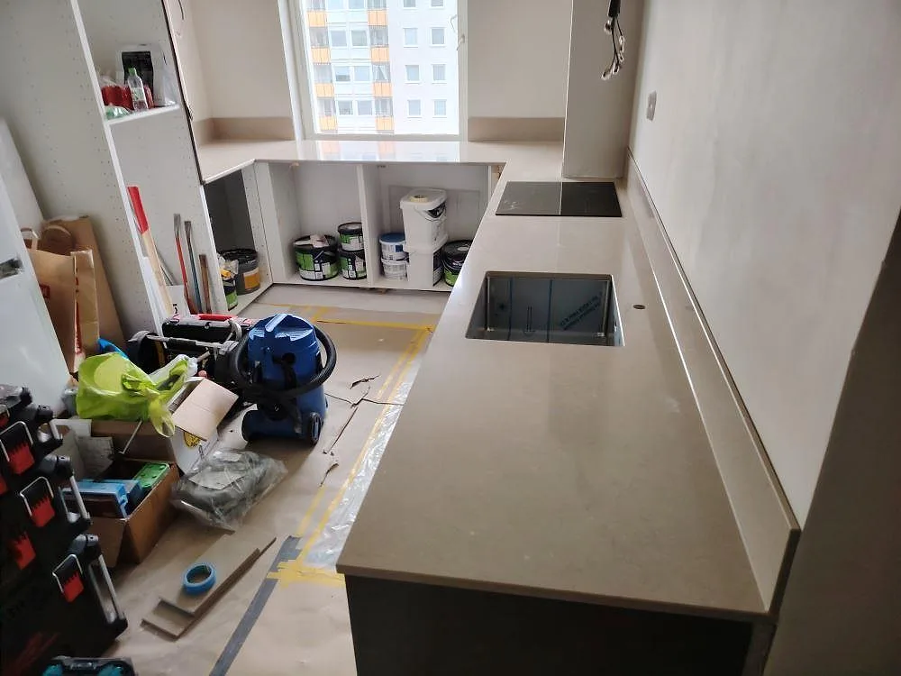 Köksbänkskiva i gråbeige Silestone Coral Clay kvartskomposit i Täby, med Polerad och Mocka enligt ordern, låg stänkskyddskant, diskhoöppning och häll under montering.