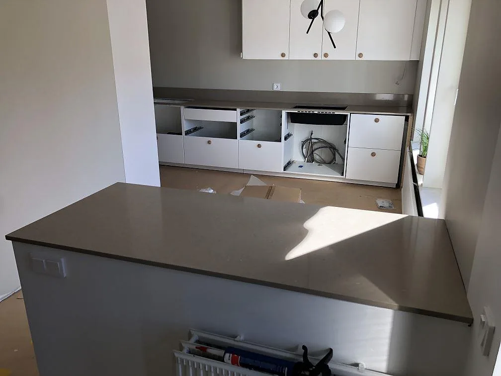 Greige köksbänkskiva i Silestone Coral Clay på halvö och vägghängd köksdel under montering i ett kök i Trelleborg.