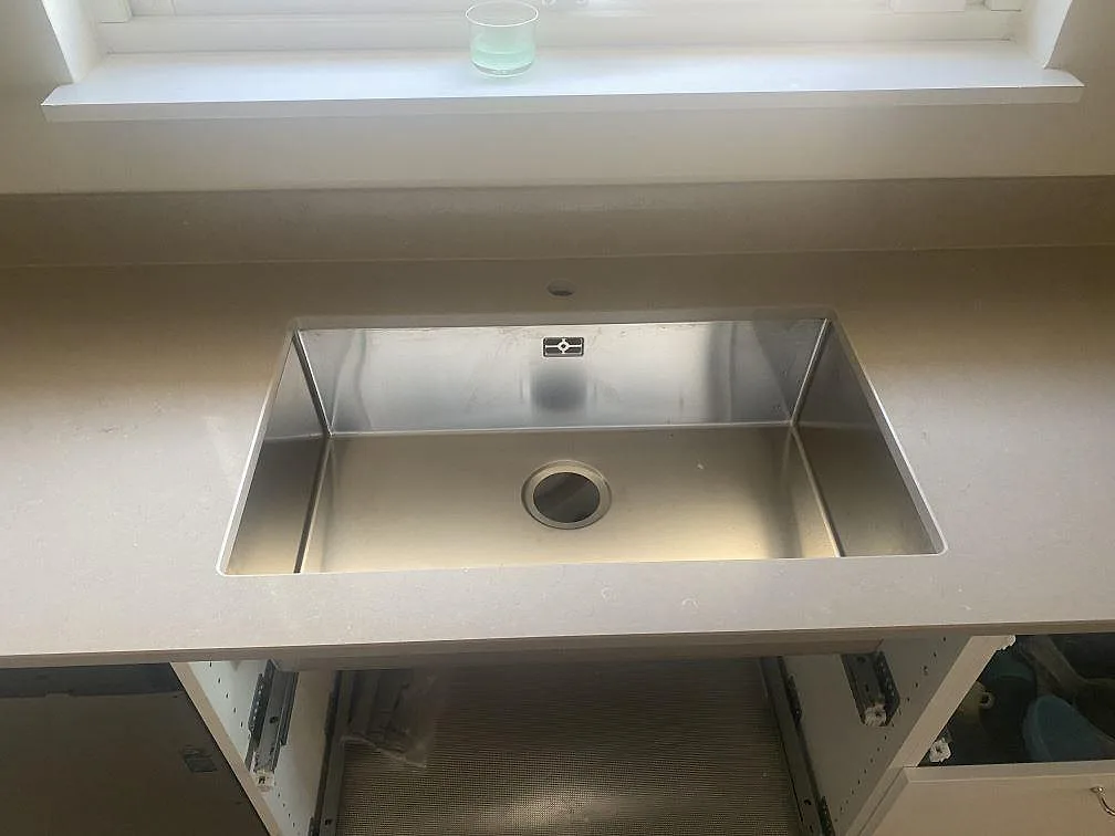 Underlimmad rostfri diskho i polerad Silestone Coral Clay köksbänkskiva framför fönster i Trelleborg.