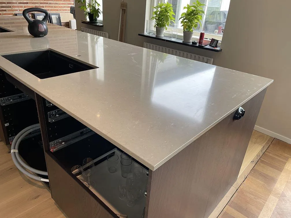 Köksö i Silestone Coral Clay, polerad komposit, med svart diskho och mörka stommar under montering i Trelleborg.