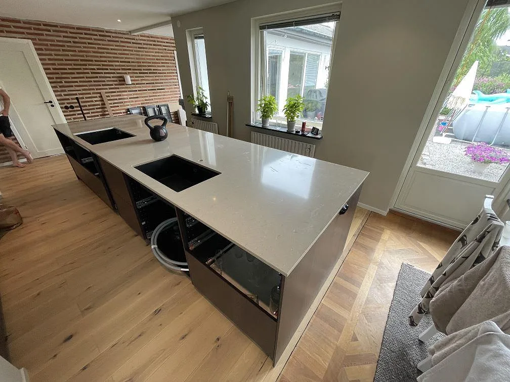 Stor köksö med köksbänkskiva i polerad Silestone Coral Clay, svart diskho och svart häll i ett kök i Trelleborg.