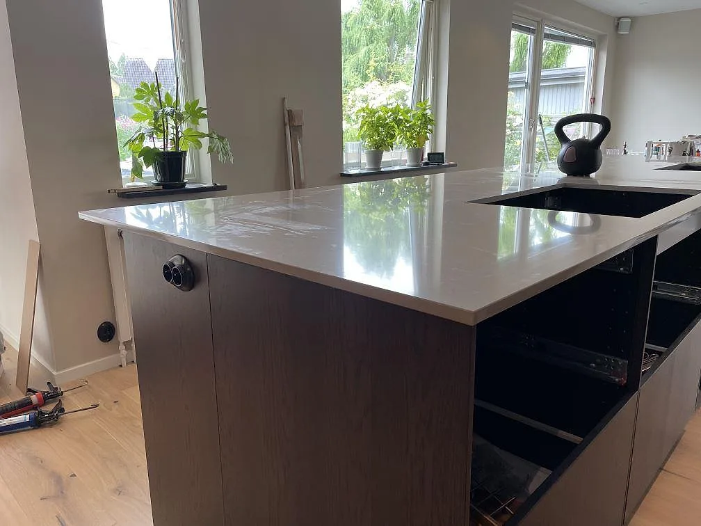 Polerad köksbänkskiva i Silestone Coral Clay på mörk köksö med svart häll och fönsterljus i Trelleborg.