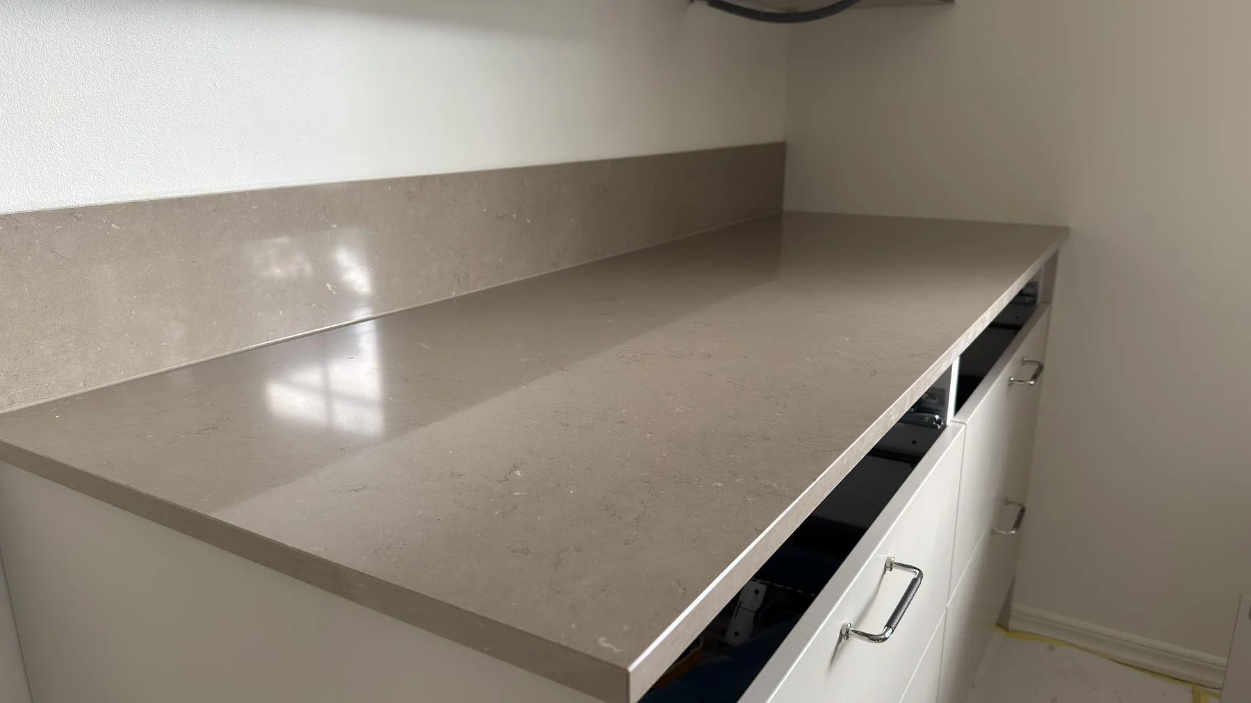 Detalj av köksbänkskiva i polerad Silestone Coral Clay, varmgrå kvartskomposit, med uppvikt stänkkant och ljus reflektion i Tumba.