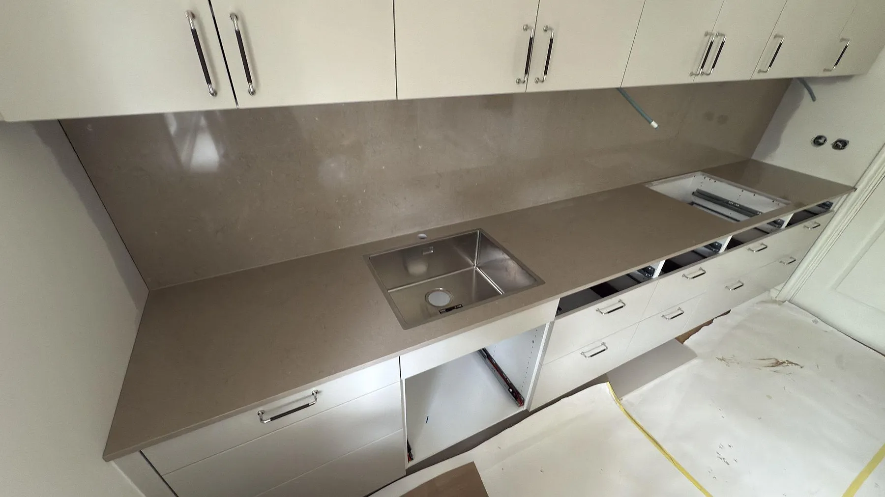 Polerad Silestone Coral Clay som köksbänkskiva i kvartskomposit med rostfri diskho, hällurtag och hög väggbeklädnad i ett kök i Tumba.