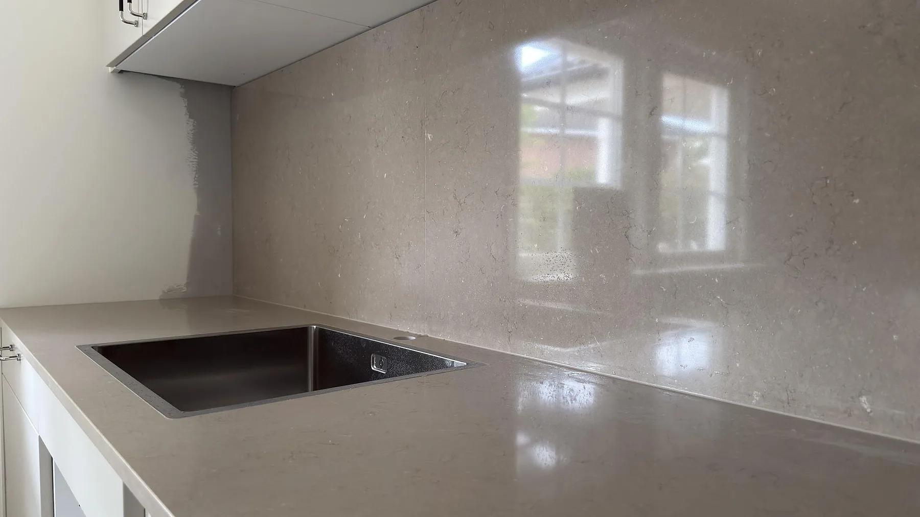 Närbild av polerad Silestone Coral Clay i kvartskomposit med rostfri diskho och blank väggbeklädnad som speglar fönstret i ett kök i Tumba.