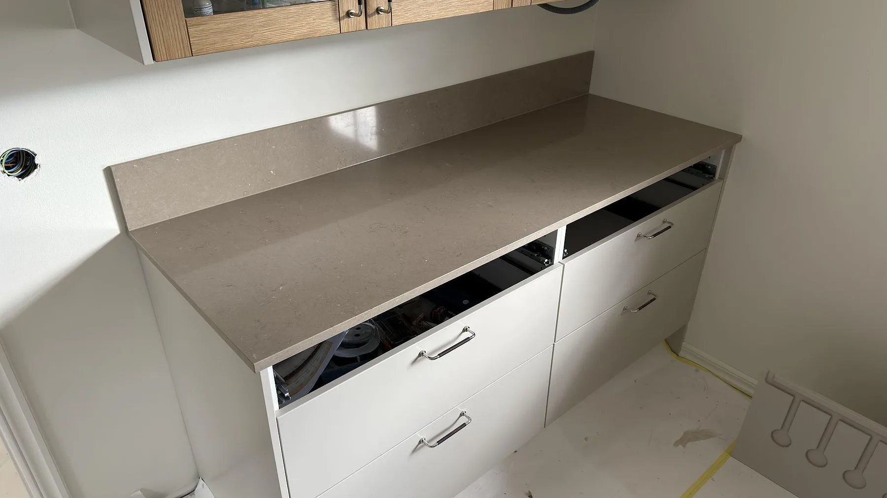 Sidovy av köksbänkskiva i polerad Silestone Coral Clay, kvartskomposit, med låg stänkkant över vita kökslådor i Tumba.
