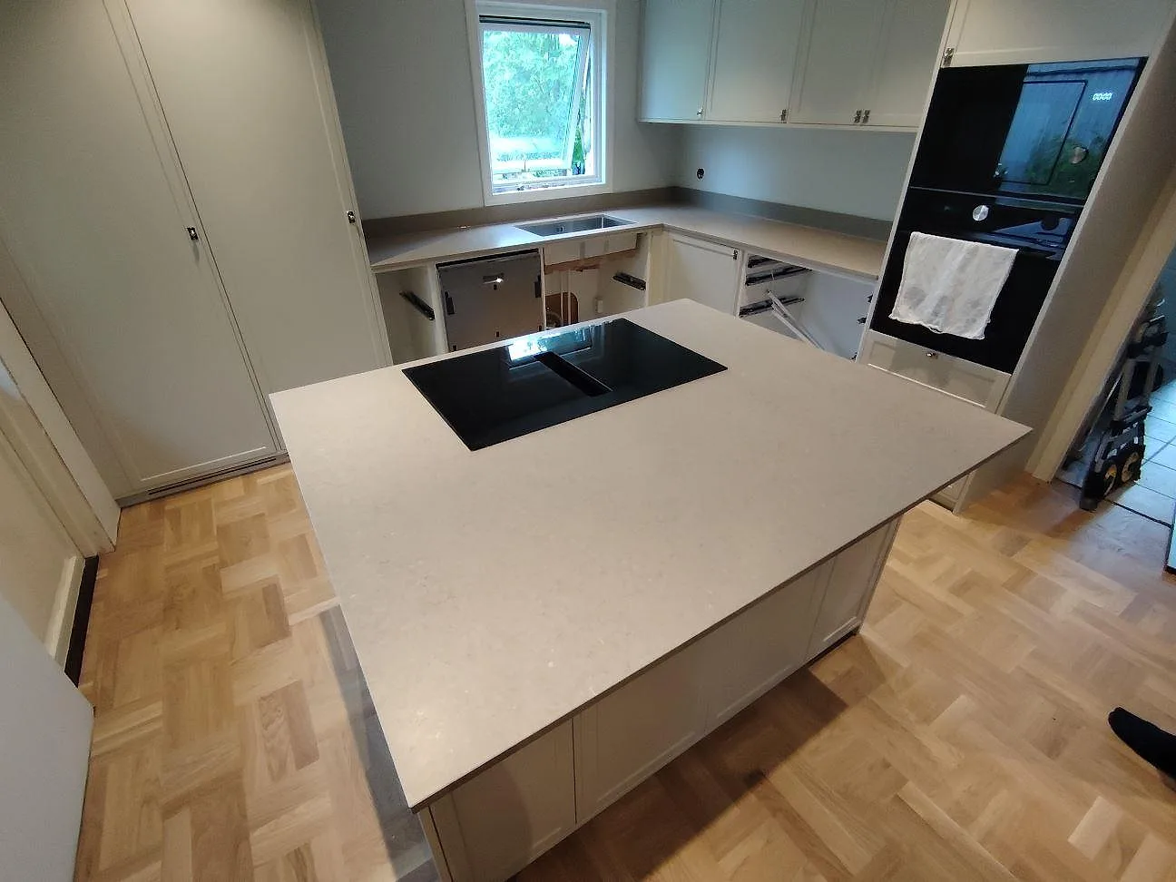 Köksbänkskiva i greige Silestone Coral Clay kvartskomposit, matt Mocka, med stor köksö och induktionshäll i ett kök i Tyresö.