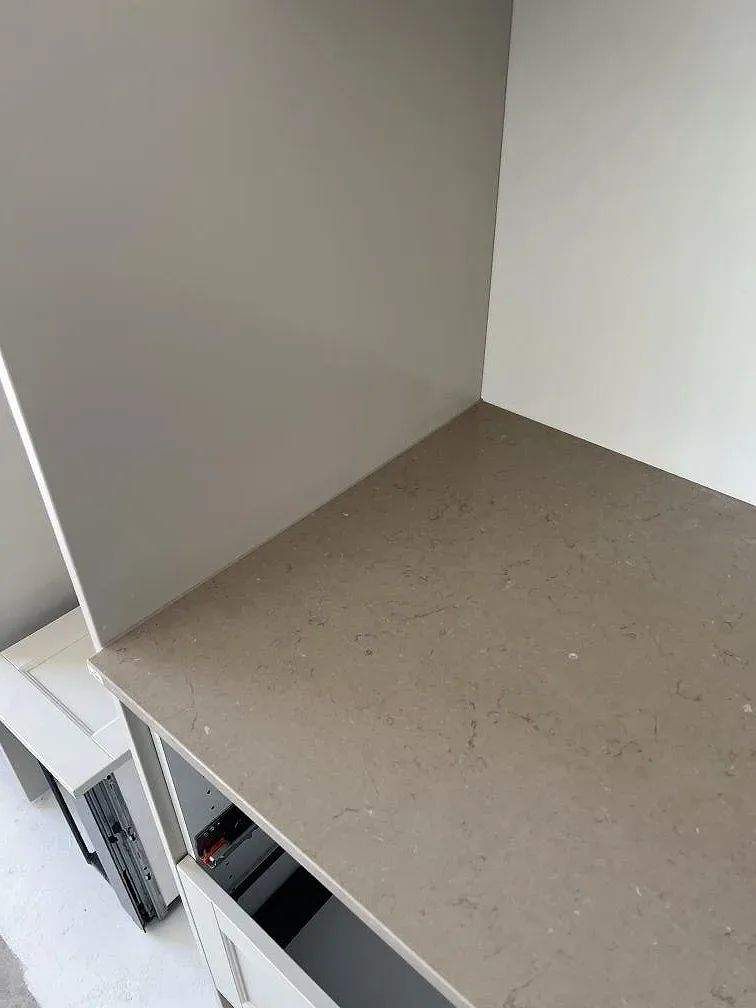 Närbild av greige Silestone Coral Clay som köksbänkskiva mot vägg och vita stommar i Ucklum.