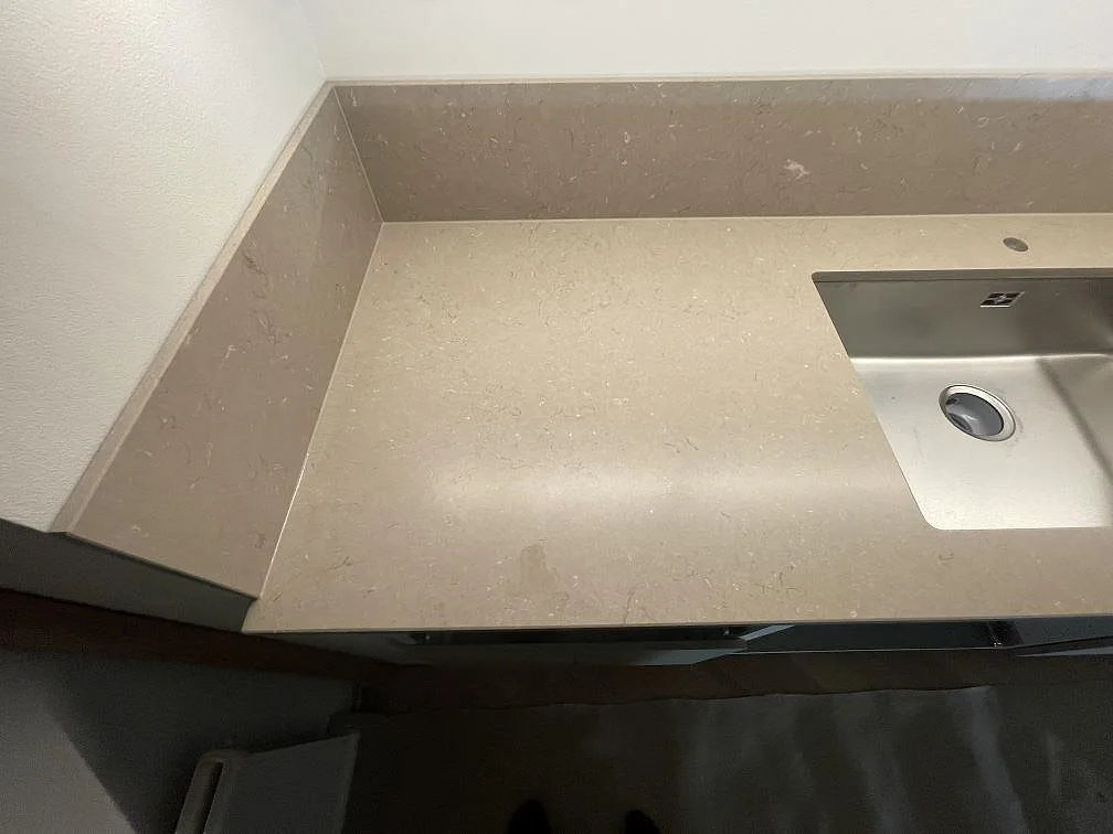 Detalj av bänkskiva och stänkskydd i Silestone Coral Clay, matt beige kvartskomposit, vid diskhozonen i ett kök i Uppsala.
